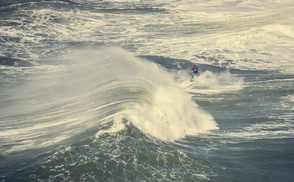 Image of a wave crashing and person riding a jetski in Nazare, Portugal